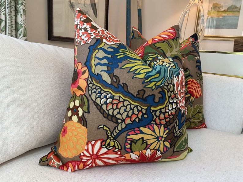 K&ouml;nnte beinhalten: Zwei dekorative Kissen mit braunem Hintergrund und einem bunten Drachen- und Blumenmuster.