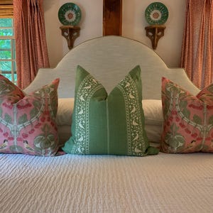 May include: A white upholstered headboard with a curved top, featuring three pillows. Two pillows have a pink and green floral pattern with small birds, and the center pillow is green with white bird designs.