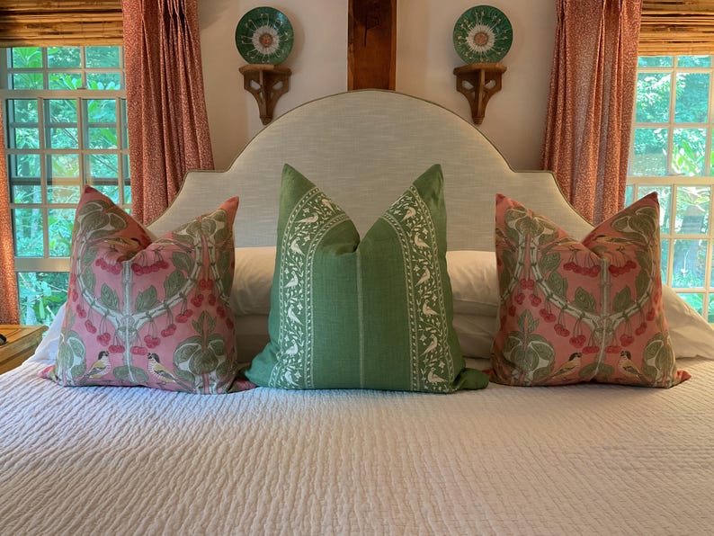 May include: A white upholstered headboard with a curved top, featuring three pillows. Two pillows have a pink and green floral pattern with small birds, and the center pillow is green with white bird designs.