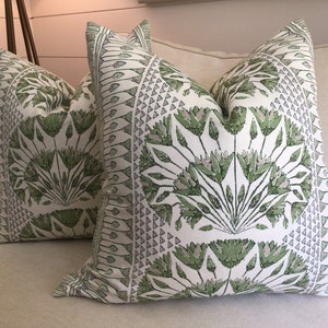 Puede incluir: Dos almohadas decorativas con fondo blanco y un patrón floral verde y gris. Las almohadas están en un sofá beige.