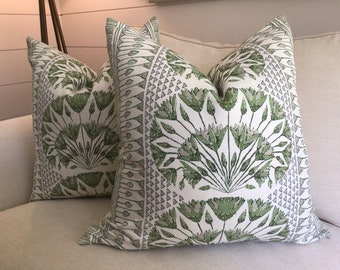 May include: Two decorative throw pillows with a white background and a green and gray floral pattern. The pillows are on a beige couch.