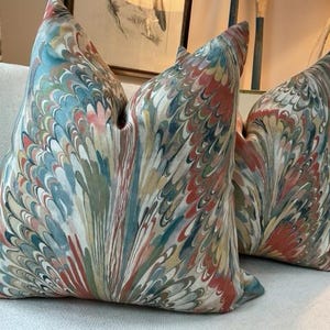 May include: Two decorative throw pillows featuring a colourful marbled pattern in shades of blue, green, red, and beige. The pillows are made from a soft, textured fabric with a subtle sheen.