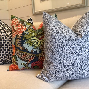 May include: Three decorative throw pillows on a cream colored couch. The pillows are all rectangular and have different patterns. The pillow on the left has a black and white geometric pattern. The middle pillow has a colorful floral pattern with a dragon design. The pillow on the right has a white background with a blue and white speckled pattern.