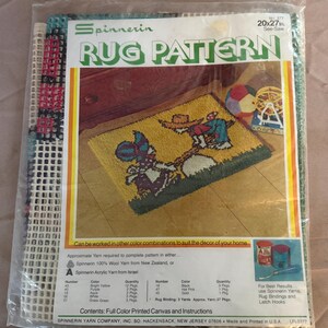 May include: A Spinnerin rug pattern kit in a clear plastic bag, featuring a 20x27 inch printed canvas. The packaging displays a finished rug design with two figures on a seesaw, yarn color requirements, and instructions for a latch hook project.