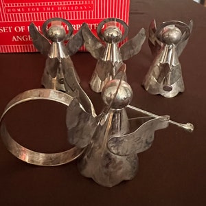 Puede incluir: Conjunto de cinco anillos de servilleta de &aacute;ngel de plata con halo y alas. Los &aacute;ngeles est&aacute;n dispuestos en c&iacute;rculo con un anillo de plata en el centro.