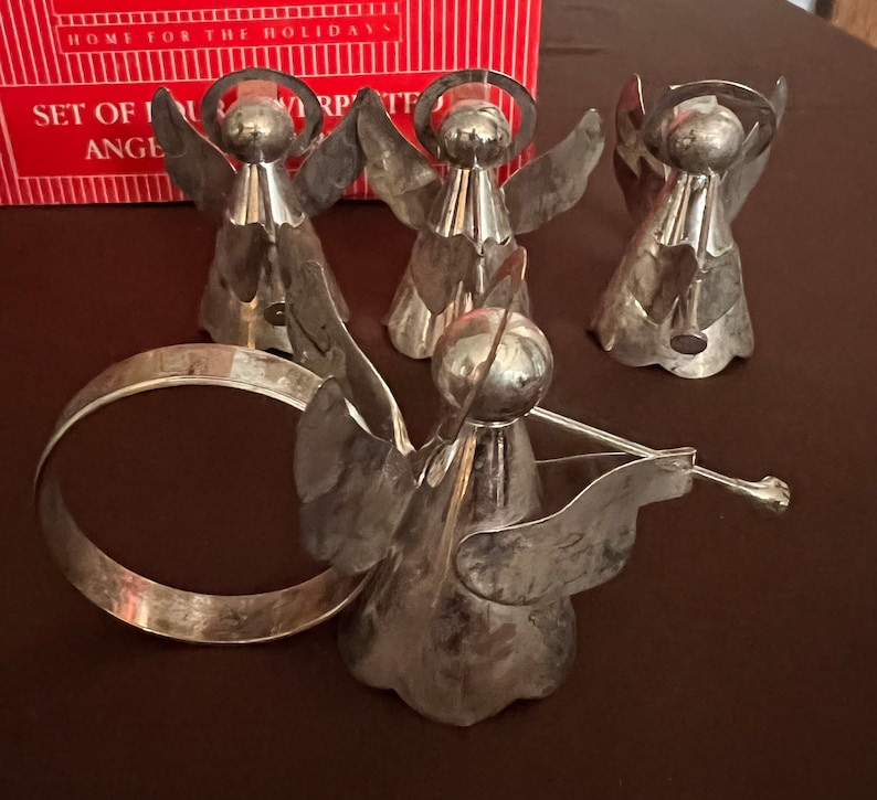 Puede incluir: Conjunto de cinco anillos de servilleta de &aacute;ngel de plata con halo y alas. Los &aacute;ngeles est&aacute;n dispuestos en c&iacute;rculo con un anillo de plata en el centro.