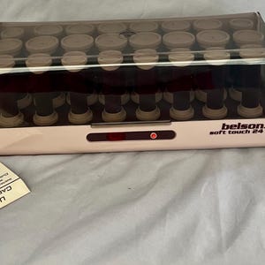 May include: A vintage Belson Soft Touch 24 hair roller set. The set includes a pink and clear plastic heating unit filled with rollers, a smaller pink case, and a user manual. The heating unit has the text "belson soft touch 24".