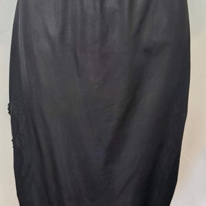 May include: Black slip skirt with a smooth, satin-like texture. The skirt has a fitted waist and falls to the mid-calf. Delicate lace trim adorns the hemline and a small section on the side. The garment is designed for layering.