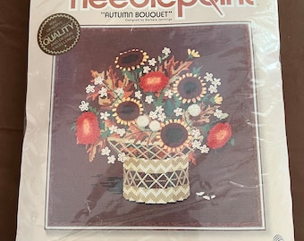 May include: A needlepoint kit featuring a colourful autumn bouquet of sunflowers, red and yellow flowers in a woven basket. The kit includes 100% cotton canvas, 100% wool yarn, a needle, a full-colour print, and instructions. "Sunset Needlepoint" and "Autumn Bouquet" are printed on the packaging.