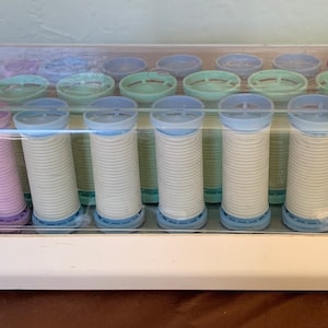 Op de afbeelding: Witte elektrische warmte rollers met een doorzichtig plastic deksel. De rollers zijn in verschillende tinten blauw en paars.