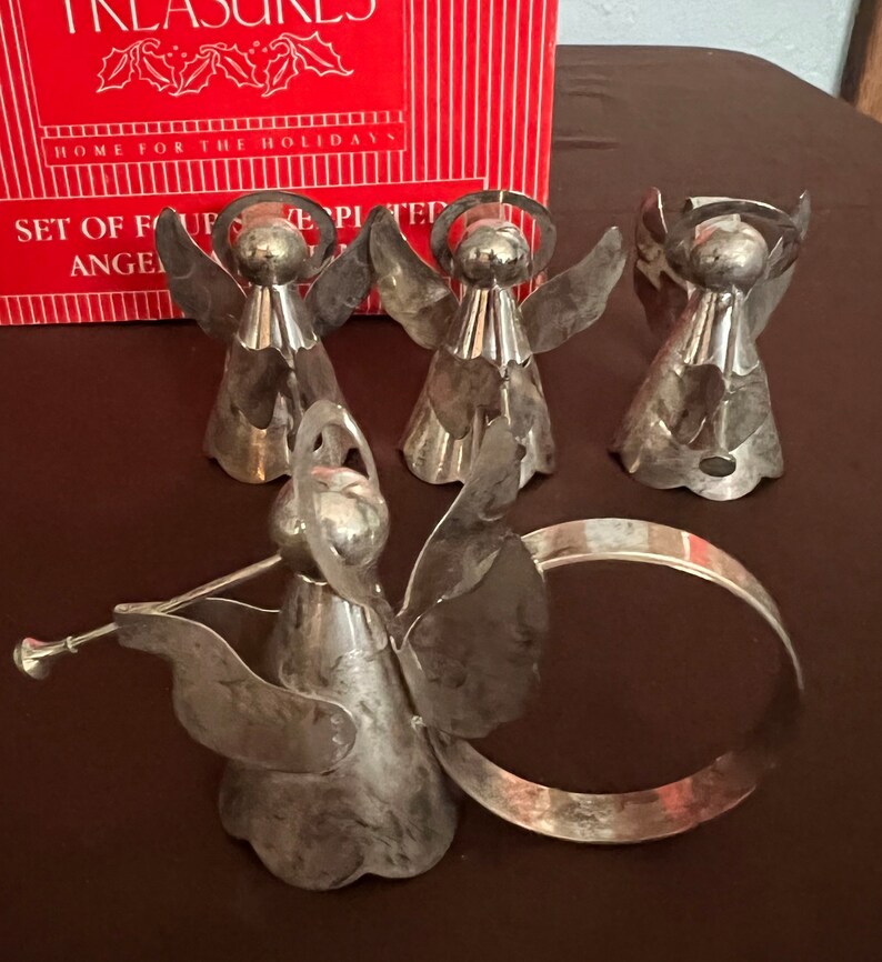 Puede incluir: Conjunto de cinco anillos de servilleta de &aacute;ngel de plata. Los &aacute;ngeles sostienen trompetas y tienen halos. Los anillos est&aacute;n en una caja que dice "Home for the Holidays" y "Set of Four Silver Plated Angel Napkin Rings".