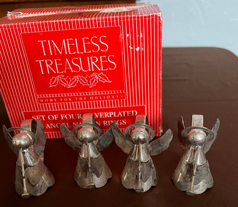 Puede incluir: Conjunto de cuatro anillos de servilleta de &aacute;ngel plateados en una caja roja con las palabras "Timeless Treasures" y "Home for the Holidays". La caja tambi&eacute;n dice "Set of Four Silverplated Angel Napkin Rings".
