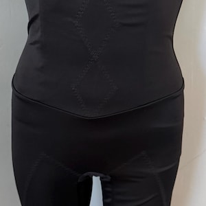 May include: A black high-waisted compression garment featuring a smooth fabric finish with subtle diamond-shaped stitching patterns on the front panel and reinforced seams along the legs, designed to provide a snug fit around the midsection.