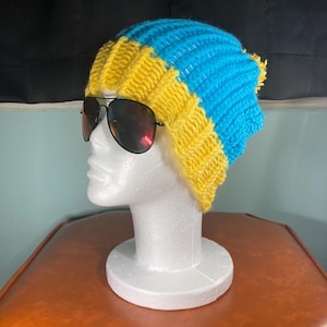 Puede incluir: Un gorro de punto azul y amarillo. El gorro está doblado hacia abajo y tiene una textura acanalada.