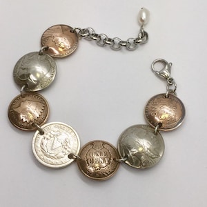 May include: A bracelet made of linked US coins, featuring a mix of copper, silver, and gold tones. The bracelet has a silver chain and a lobster clasp.