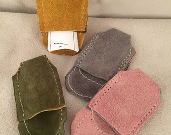 May include: Four small suede pouches in different colours: mustard yellow, grey, green, and pink. Each pouch has a flap that folds over to close the pouch.
