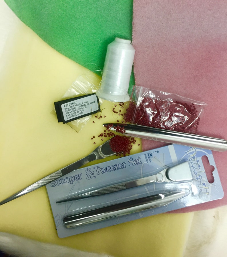 May include: A close-up of beading supplies including red seed beads, a spool of white thread, a pair of tweezers, a bead scooper, and a package of beading needles. The text on the package of needles reads "743 23031 Beading Needle No.11 Gold Eye Size 0.6MM x 52.5 MM Japanese Quality Carp Made in Japan".