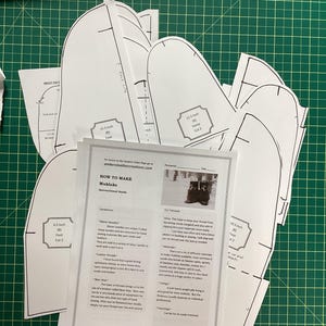 Op de afbeelding: Een set witte papieren patronen voor het maken van mukluks, met instructies over hoe je ze kunt maken. De patronen omvatten verschillende maten voor de voet, vamp en hiel. De instructies bevatten informatie over de benodigde materialen, zoals leer, draad en pees.