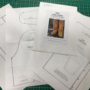 Può includere: Un set di modelli di carta bianca per la realizzazione di mocassini. I modelli sono etichettati "Voyager Mukluk Pattern" e includono istruzioni per tagliare la pelle e cucire. Il modello è di Ambers Leather Creations.