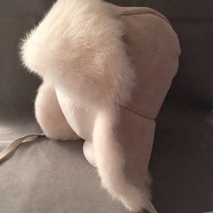 May include: A white faux fur trapper hat with a suede crown and ear flaps. The hat has a long tie that can be tied under the chin.