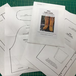 Könnte beinhalten: Ein Satz weißer Papiermuster zum Nähen von Mokassins. Die Muster sind mit "Voyager Mukluk Pattern" beschriftet und enthalten Anweisungen zum Zuschneiden von Leder und Nähen. Das Muster stammt von Ambers Leather Creations.