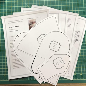 May include: A set of white paper patterns for making gauntlets. The patterns are labelled with instructions for cutting and sewing. The text on the paper says "How to Make Gauntlets pt. 1 Instructional Guide".
