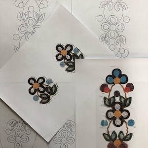 Op de afbeelding: Vier vellen papier met zwart-witte lijntekeningen van bloemmotieven. Een vel heeft een geborduurd bloemmotief in tinten bruin, wit, blauw en oranje.