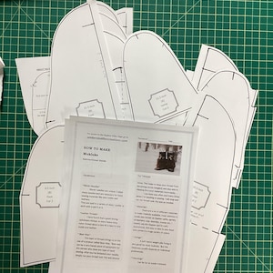 Peut inclure: Un ensemble de patrons en papier blanc pour la fabrication de mukluks, avec des instructions sur la façon de les réaliser. Les patrons comprennent des mesures en pouces et sont étiquetés avec des noms comme "Pied" et "Vamp".