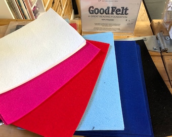 May include: A stack of felt sheets in various colours, including white, pink, red, light blue, dark blue, and black. The felt is labelled "GoodFelt, A Great Beading Foundation, 100% Polyester".