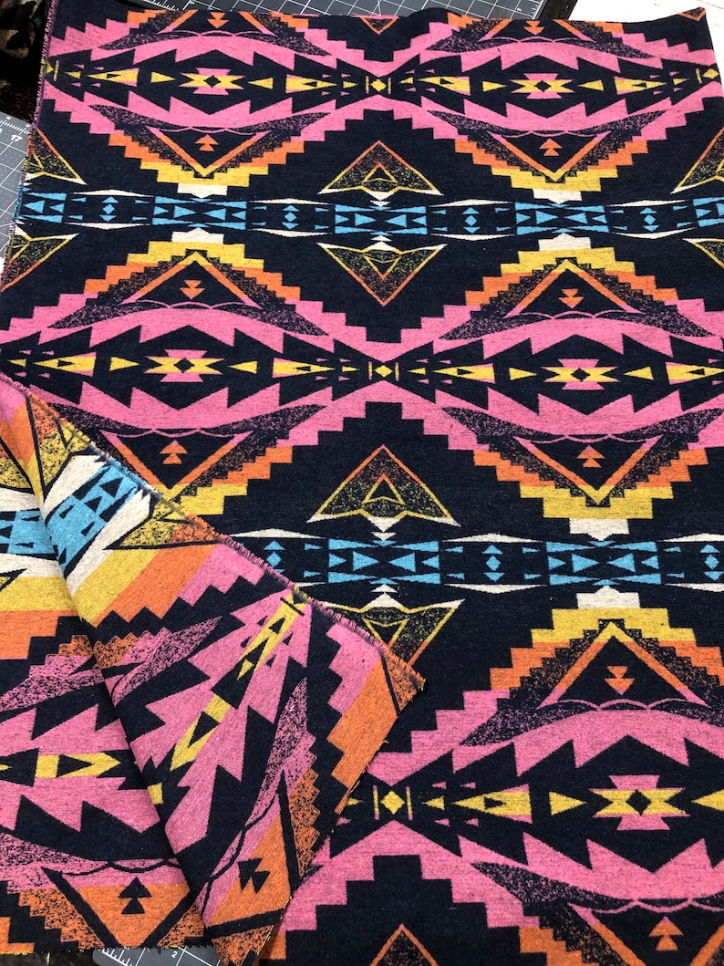 May include: A black fabric with a geometric pattern in pink, orange, yellow, and blue. The pattern is a repeating design of diamonds and triangles.