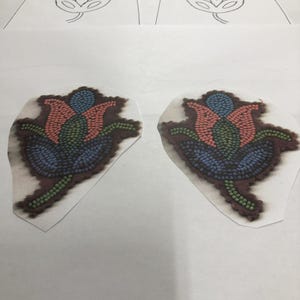 Könnte beinhalten: Zwei florale Designs, eines gezeichnet und zwei bestickt, werden auf einer weißen Oberfläche gezeigt. Die bestickten Designs zeigen eine Blume mit roten, blauen und grünen Perlen. Die gezeichneten Designs sind einfache Umrisse derselben Blume.