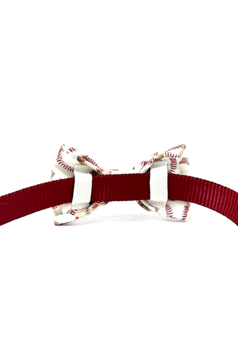 以下が含まれることがあります： 野球をテーマにしたペット用蝶ネクタイ。 蝶ネクタイは、赤い野球のステッチが入った白い生地でできており、バーガンディ色の首輪に取り付けられています。 蝶ネクタイは首輪の中央に配置され、対称的なデザインになっています。