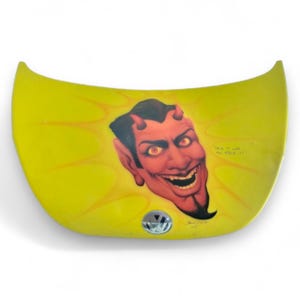 May include: Yellow car hood with a red devil face airbrushed on it. The devil is smiling and has horns. The text "Drive it like you stole it" is written on the hood. The hood has a Volkswagen logo.