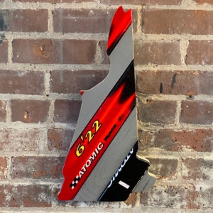 May include: A gray and red wooden sign shaped like a state with the text "6'22 ATOMIC" printed on it.