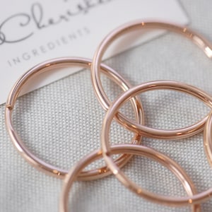 May include: Five rose gold metal rings interlocked together. The rings are smooth and shiny.