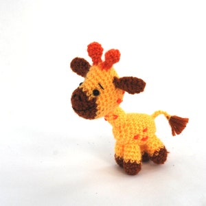 May include: A handmade crochet giraffe toy in shades of yellow, orange, and brown. The giraffe has small orange spots, brown hooves, and a brown tail. The toy is approximately 5 inches tall.
