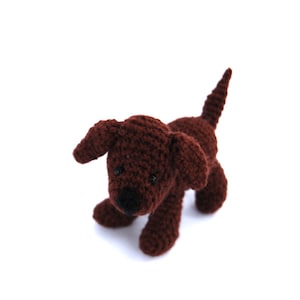 Op de afbeelding: Een bruin gehaakt puppy speelgoed met zwarte ogen. Het speelgoed staat op een witte achtergrond.