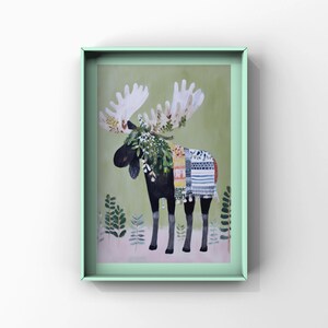 May include: A framed art print of a black moose with large white antlers. The moose is adorned with a colorful blanket and a wreath of greenery. The background is a soft green with stylized plant illustrations, all within a mint green frame.