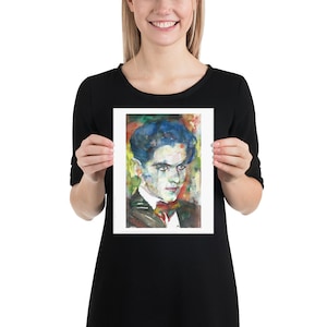 May include: A watercolour painting of a man with blue hair and a colourful background. The man is wearing a dark suit with a white shirt and a bow tie. The painting is framed in a white frame.