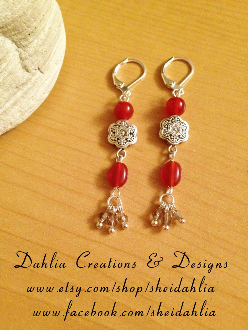 May include: A pair of silver earrings with red gemstone beads and a silver flower charm. The earrings have a dangling design with a cluster of small silver beads at the bottom.