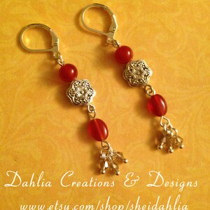 May include: A pair of silver earrings with red gemstone beads and silver floral accents. The earrings have a dangling design with a cluster of small crystals at the bottom.