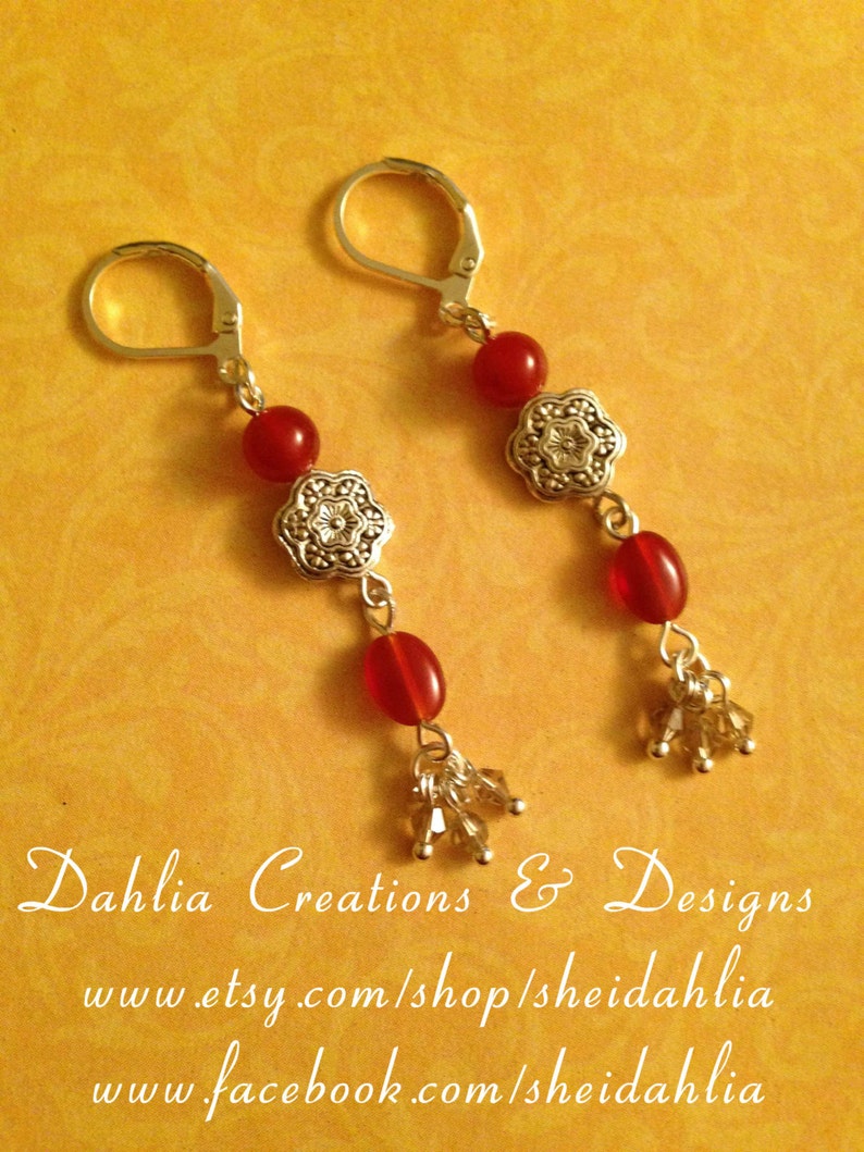 May include: A pair of silver earrings with red gemstone beads and silver floral accents. The earrings have a dangling design with a cluster of small crystals at the bottom.