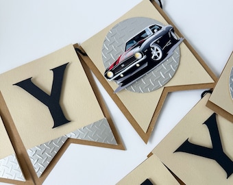 May include: A black and red car birthday banner with the word "Happy" and a black car on a silver background. The banner is made of brown cardstock with silver diamond-shaped accents.