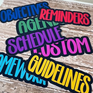 May include: A collection of colorful, die-cut labels with various words in bold, bubble letters. The labels include "OBJECTIVES," "REMINDERS," "AGENDA," "SCHEDULE," "CUSTOM," "HOMEWORK," and "GUIDELINES." Each label has a black border.