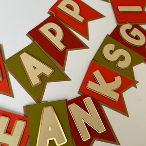 May include: A banner with the words "Happy Thanksgiving" in gold letters on a red and green background. The letters are layered and have a 3D effect.