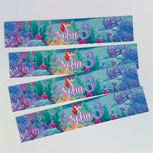 Puede incluir: Cuatro etiquetas de botella de agua azules y verdes con una ilustraci&oacute;n de sirena y el texto "Sofia 3" en morado.