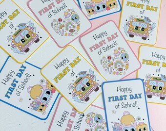 May include: A set of ten colorful cards with the text "Happy First Day of School!" and various illustrations of school supplies, a bus, and a backpack. The cards are printed on white cardstock with a light pink, light blue, or yellow border.