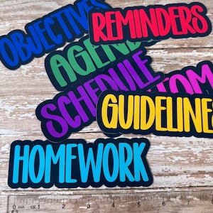 May include: A collection of colorful stickers with black borders and various words in bold, sans-serif fonts. The words include "OBJECTIVES," "REMINDERS," "AGENDA," "SCHEDULE," "GUIDELINES," and "HOMEWORK." A ruler is at the bottom.