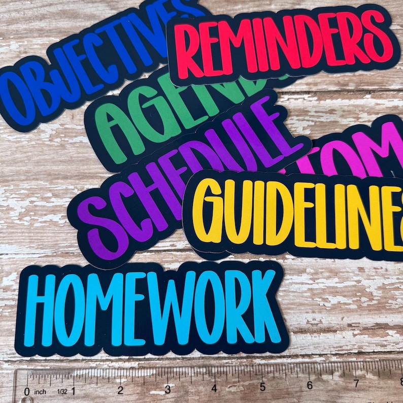 May include: A collection of colorful stickers with black borders and various words in bold, sans-serif fonts. The words include "OBJECTIVES," "REMINDERS," "AGENDA," "SCHEDULE," "GUIDELINES," and "HOMEWORK." A ruler is at the bottom.