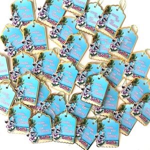 May include: A collection of light blue gift tags with a beach theme. Each tag has the words "THANK YOU FOR COMING! Sofia" printed on it, along with a cartoon image of a person with a drink. The tags have a scalloped edge and a green string.
